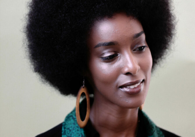 Ladan Osman in a black top with a green scarf, large earrings and a necklace