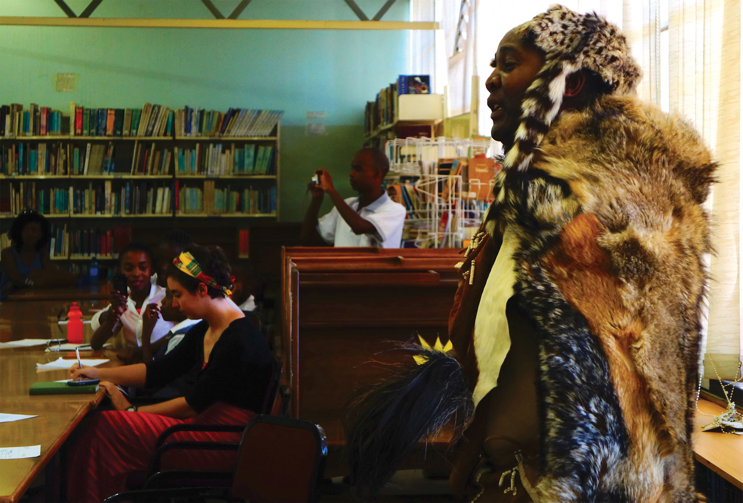 Moroka Moreri wears fur and patterned clothes, performing poetry in a room full of books