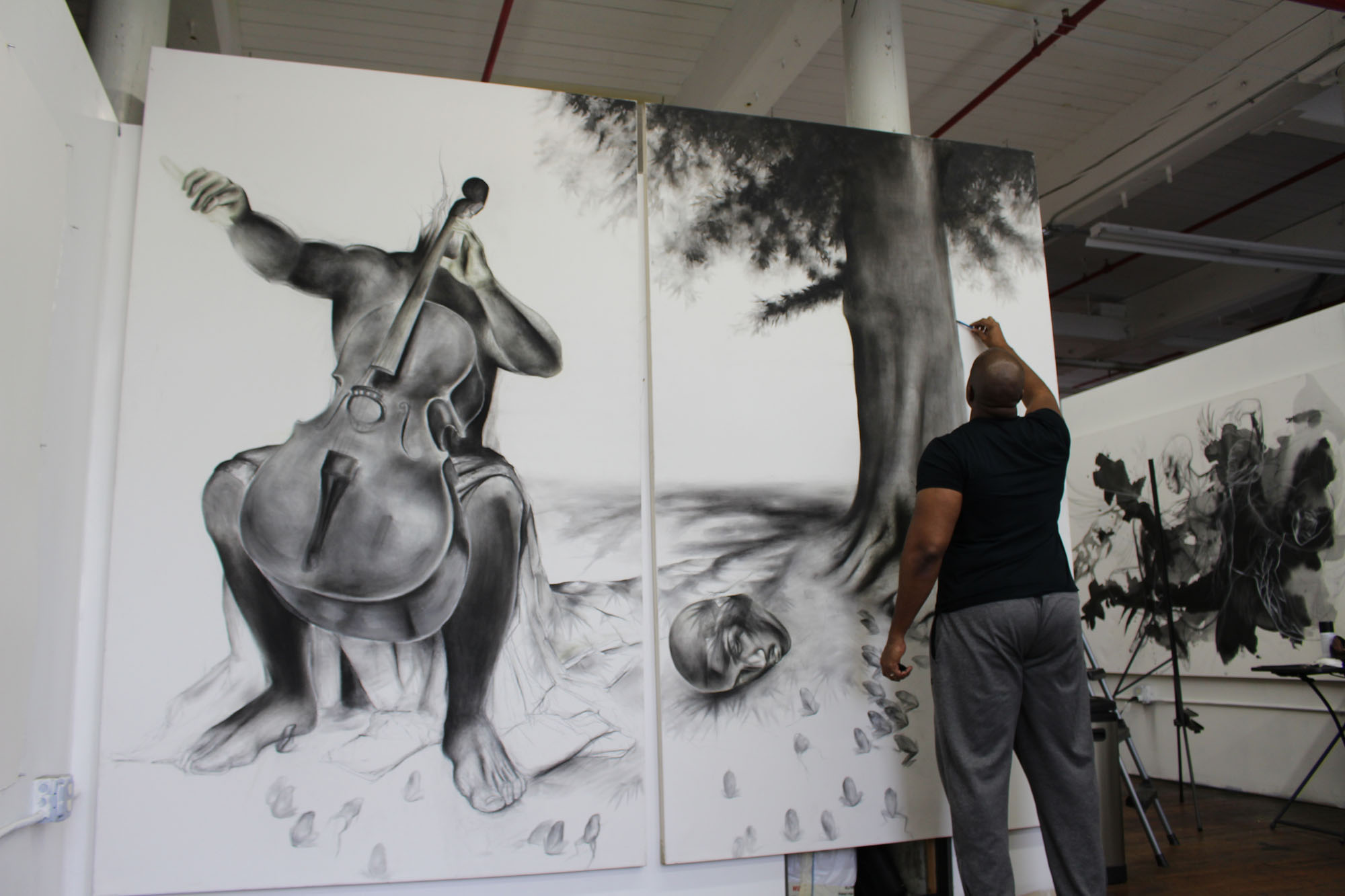 Artist Imo Imeh Nseh stands in front of a tall double canvas painting in black and white